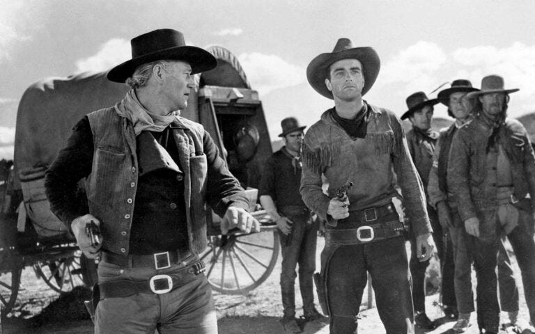 John Wayne and a group of cowboys holding guns in a black and white movie scene