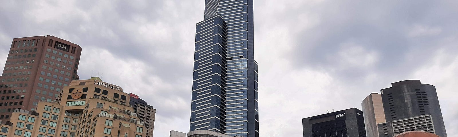 High rise office blocks and residential towers with some trees in the foreground and the Evan Walker bridge over the Yarra River