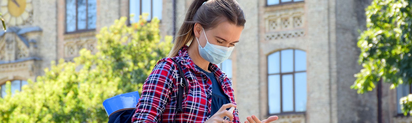 College student uses hand sanitizer while walking on college campus, wearing a face mask. Photo by Nemer-T/Getty Images