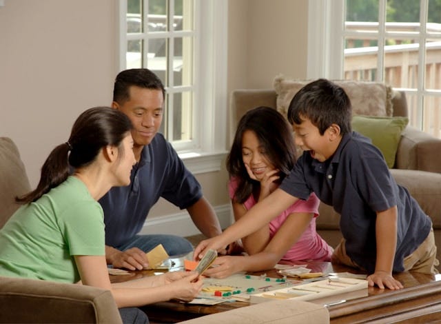 Family of four sitting around table playing Monopoly