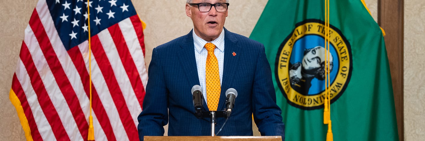 Gov. Inslee standing at a podium with flags on either side