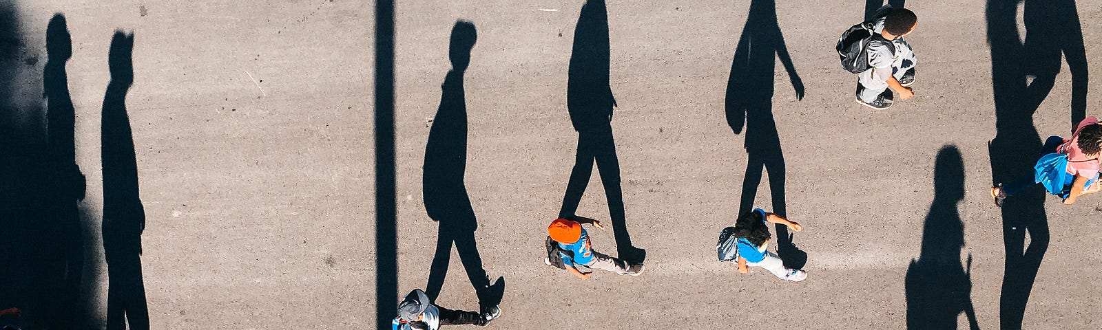 photo taken from above of people walking on the street and their large shadow silhouettes.