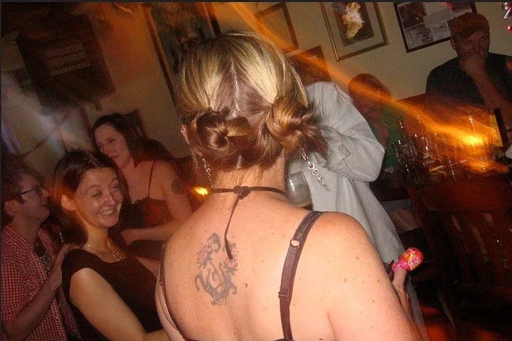 Woman with bleached pigtails and a back tattoo in a bar.
