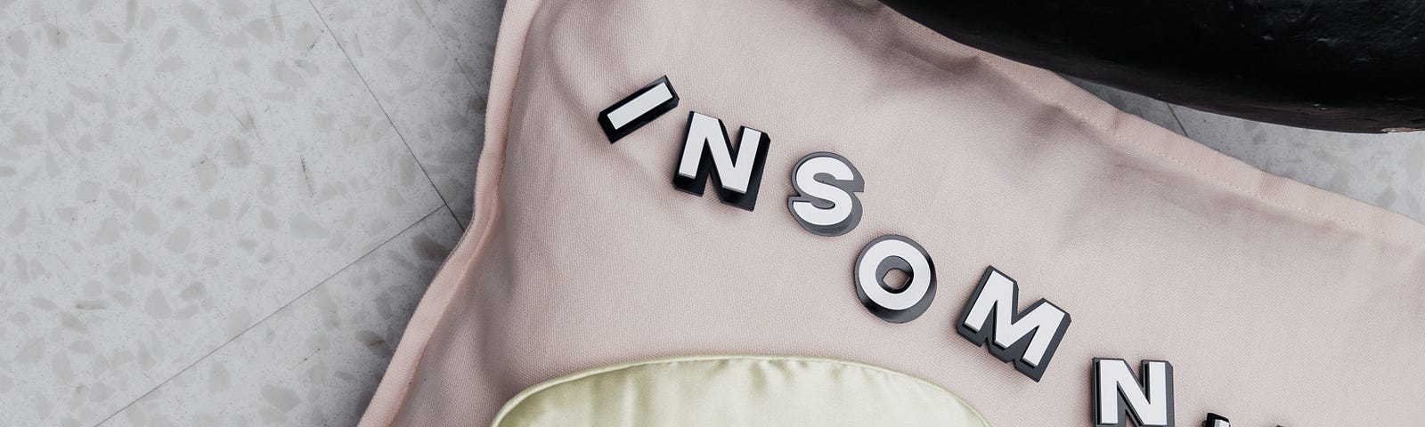 Pillow with Insomnia written on it, and a eye mask on top of it.