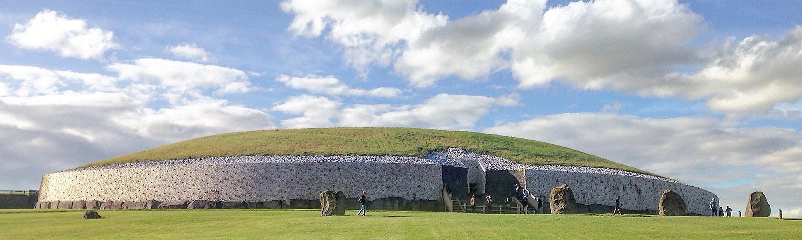 Newgrange Neolithic Passage Tomb — a huge shallow-domed edifice, edges faced in white stone and grass-topped.