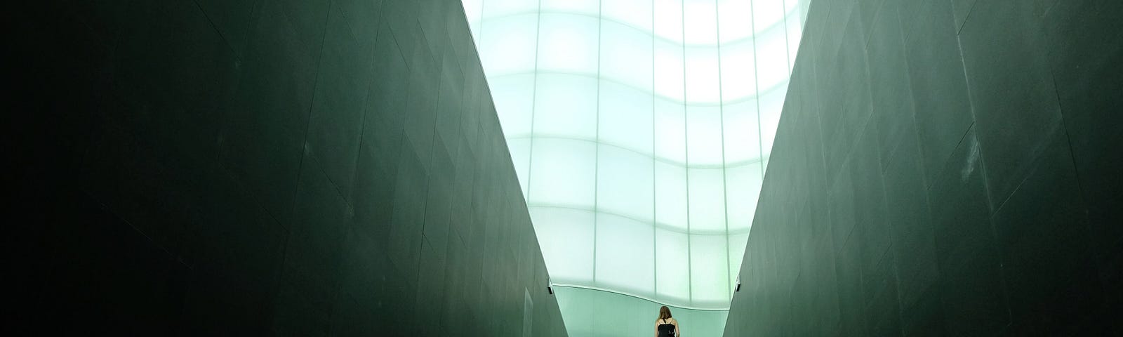 A long staircase with a person standing up at the top with a bright halo of light behind him.