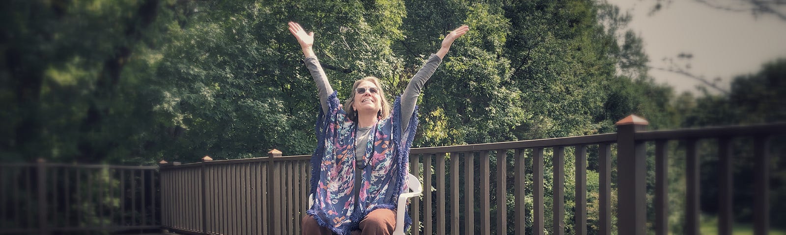 woman sitting on deck raising her hands to the sky in a gesture of happiness