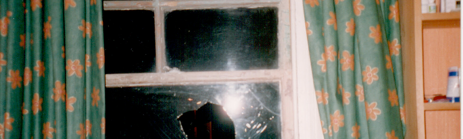 A broken window pane. There is a large hole in the window surrounded by cracks in the shatter-proof glass.