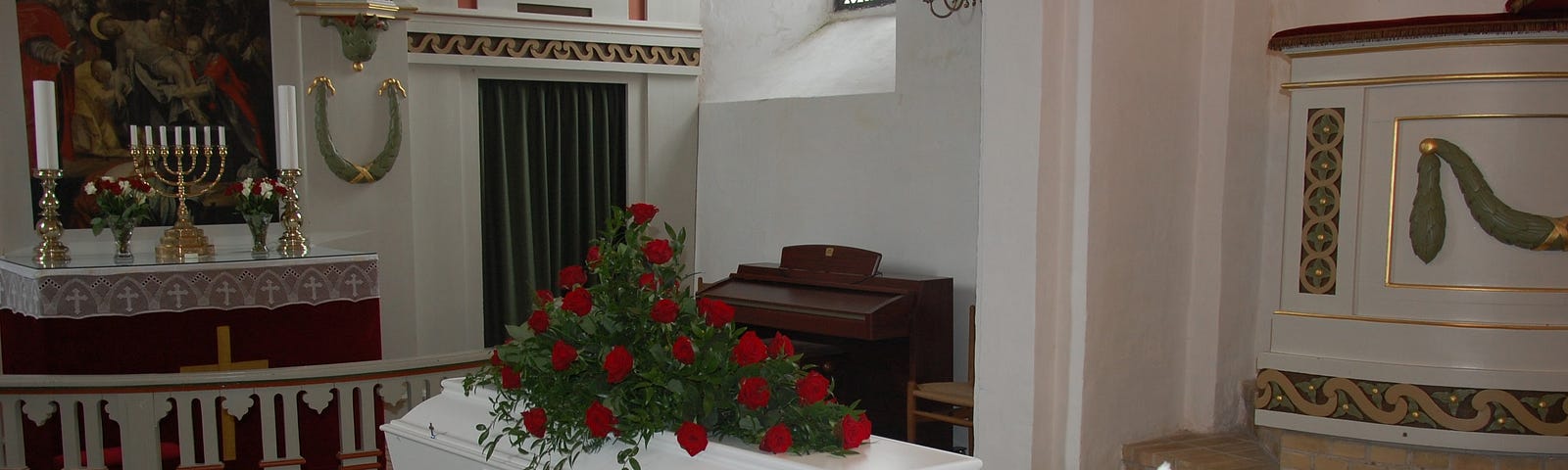 A white coffin in a church with roses on the lid.