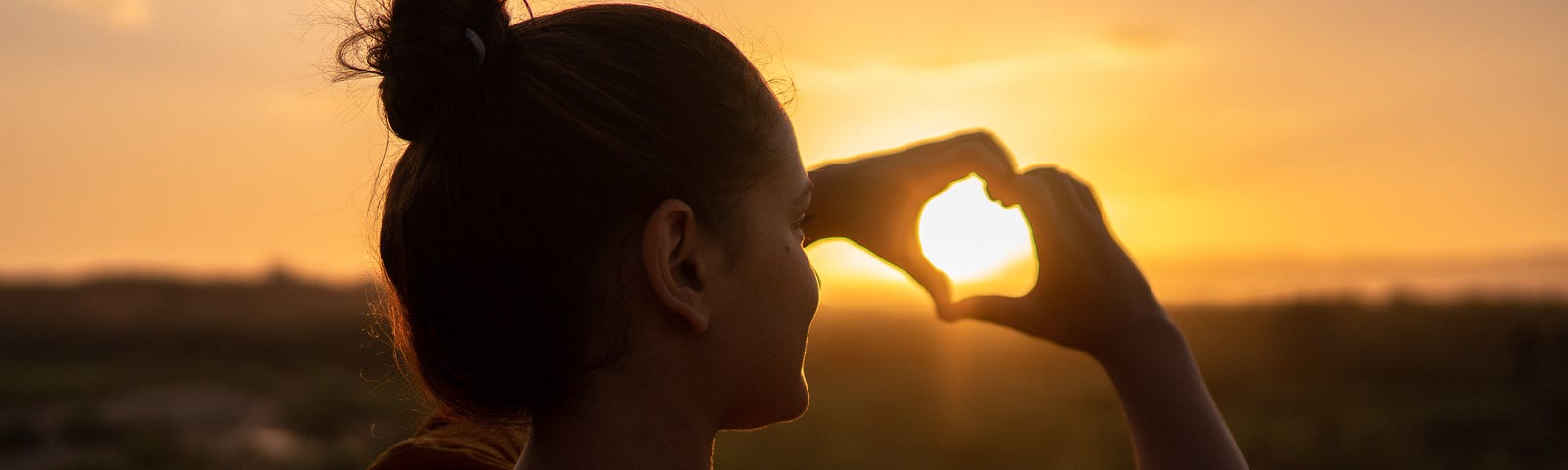 Woman making a heart sign with her hands which captures the setting sun