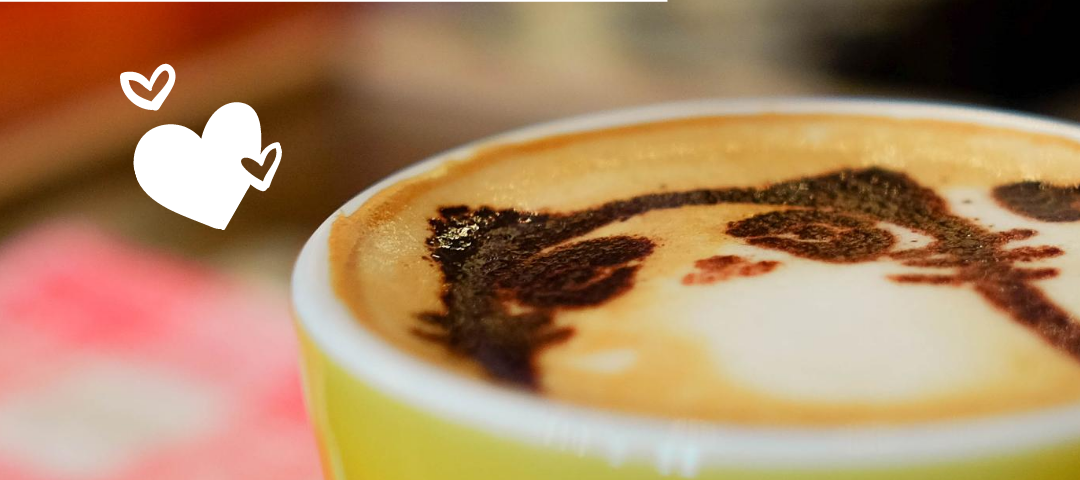 A cup of coffee with latte art featuring a cat. There are drawings of hearts beside the cup and the word Compassion.