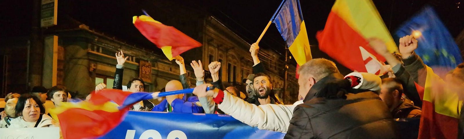 Enthusiastic protesters at night in Cluj-Napoca, Romania, waving Romanian flags and holding a banner with the message “JOS ponta JOS comunismul” (DOWN with Ponta DOWN with communism). The atmosphere is vibrant with citizens actively participating in the democratic process, calling for political change.