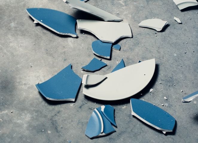 Picture of a blue plate, broken into many pieces on the ground.