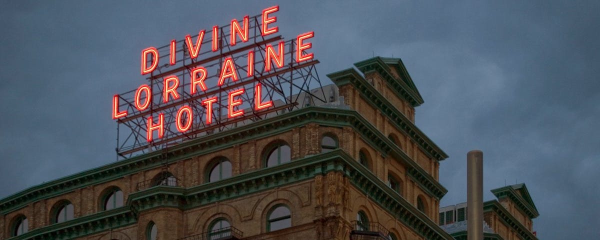 A photograph of a large 19th-century hotel with the words “Divine Lorraine Hotel” illuminated in a neon sign on its roof.