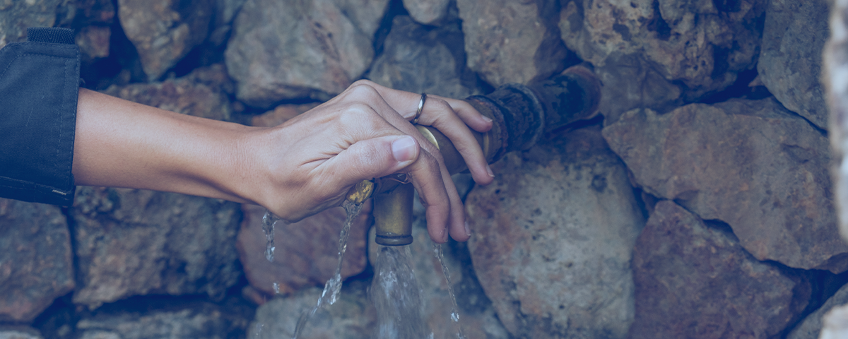 Picture showing a woman's hand opening a tap coming out of a stone wall.