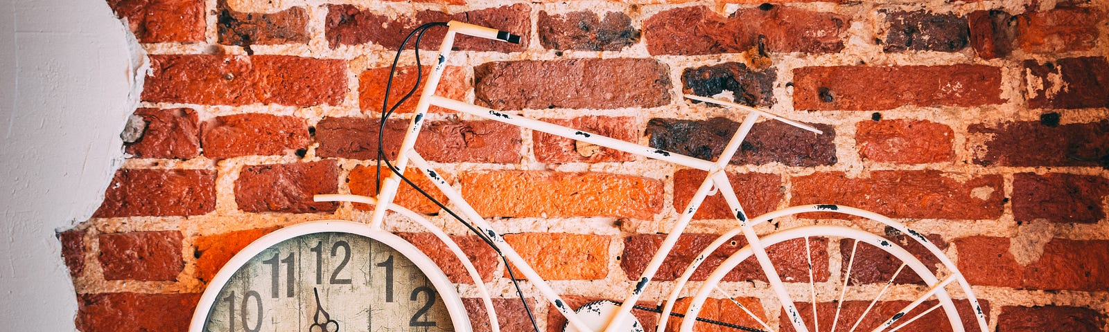 A white bicycle hangs in front of a brick wall, the front wheel is a clock