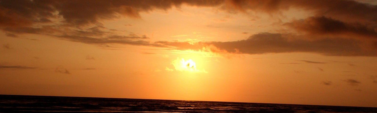 Image of a woman sitting cross-legged and raising her hand to the sunset on the beach