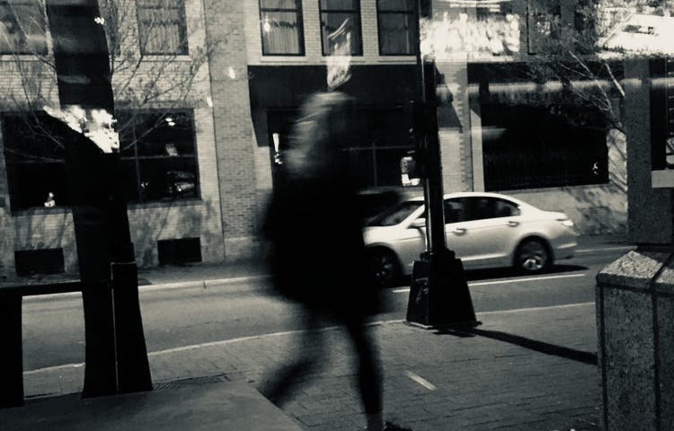 Black and white blurry shot of a stranger walking on the street while a car passes by