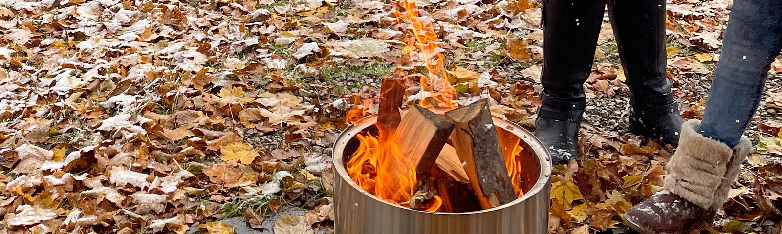 A portable bonfire unit surrounded by leaves and two people.