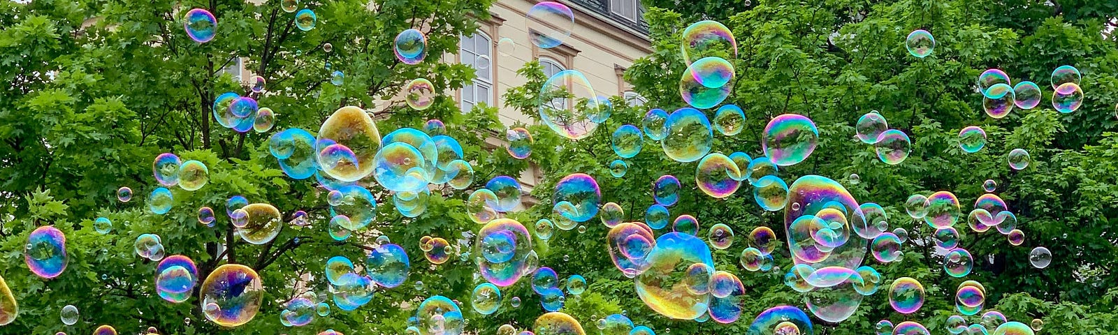 colorful soap bubbles on a background of leafed trees and a European apartment building.