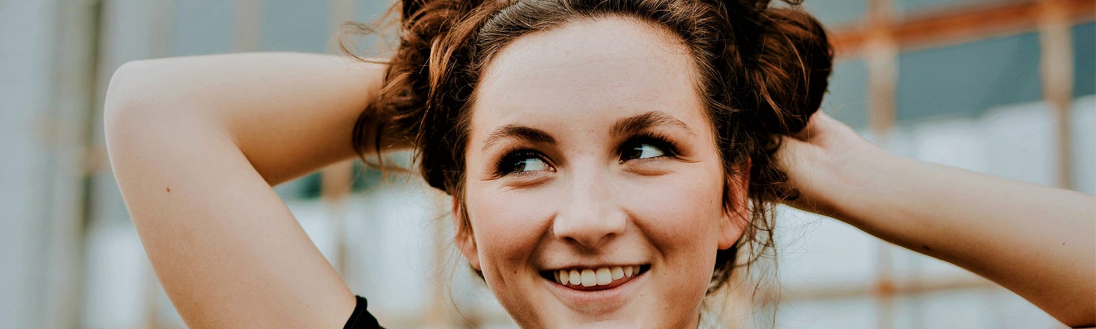 smiling girl with long brown hair tied up and arms raised behind her head