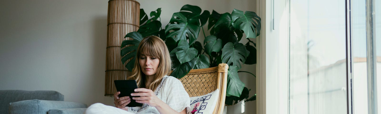 A woman sits in a chair and reads her eBook in the afternoon light.