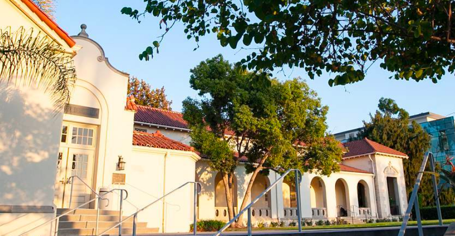 A sunny image of Whittier College is displayed, focused on the steps outside Diehl Hall on the west side. Diehl Hall is white with orange roofing, reminiscent of Spanish architecture. A tree shades the stairs in the corner of the image.