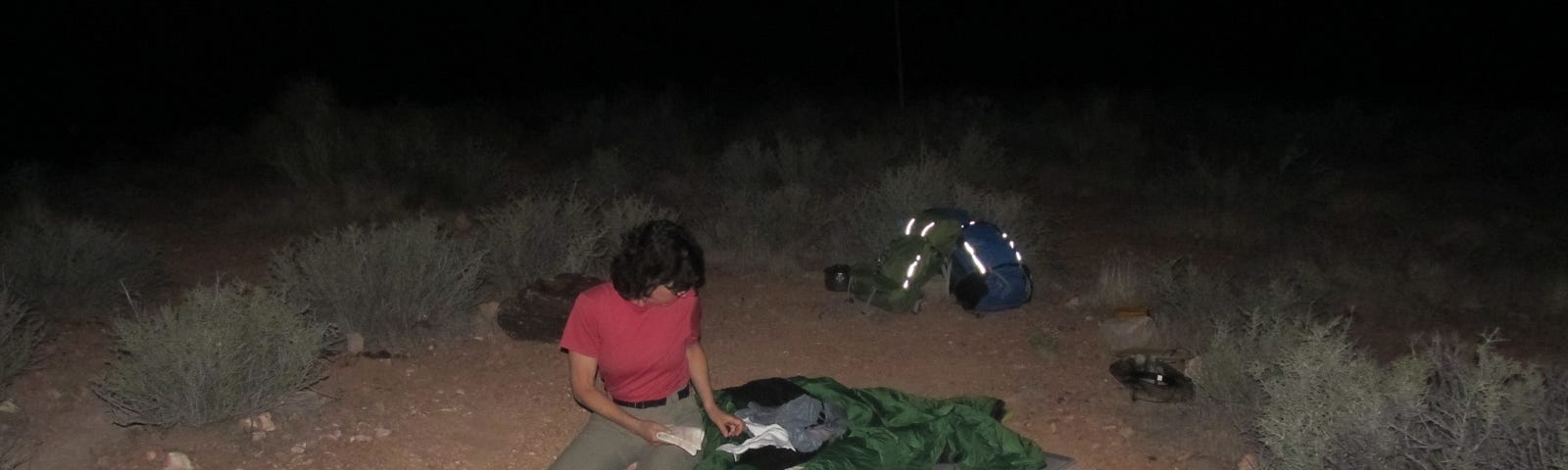 Woman kneeling on a sleeping pad on the ground in the dark night.