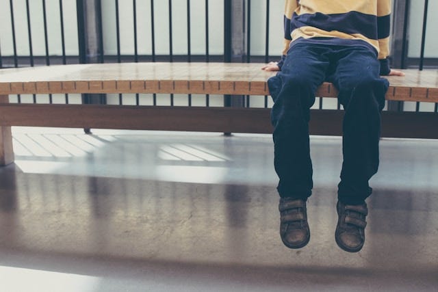 Child sits on bench, photographed from the waist down