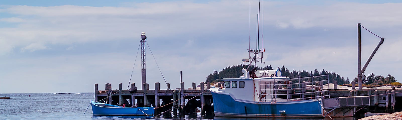 Fishing boats along a pier in the water near a point of rocks on a bright day.