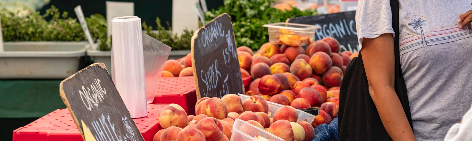 The stonefruit table at a market with a partially obscured sign saying “Organic white…”, and female shopper nearby.