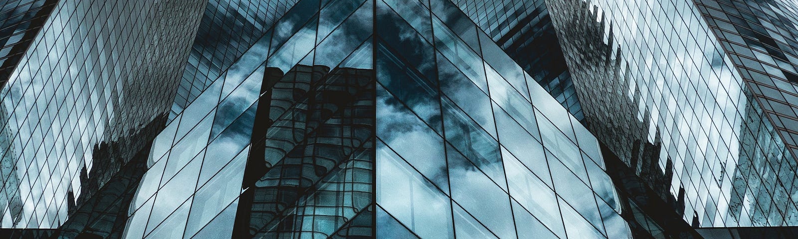 Image of tall glass office buildings with wall-to-wall windows that reflect blue sky and clouds, from the perspective of the ground looking up.