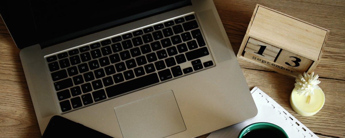 Photo of laptop on a desk with cellphone, calendar and papers.