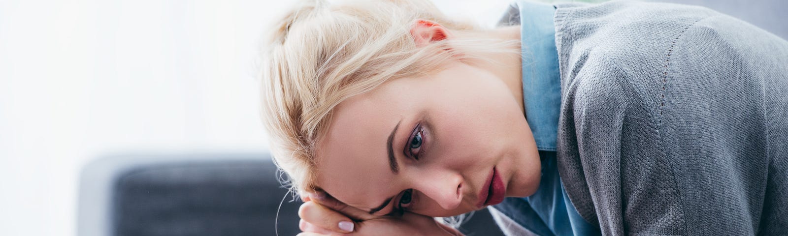 Selective focus of upset woman with folded hands sitting at home