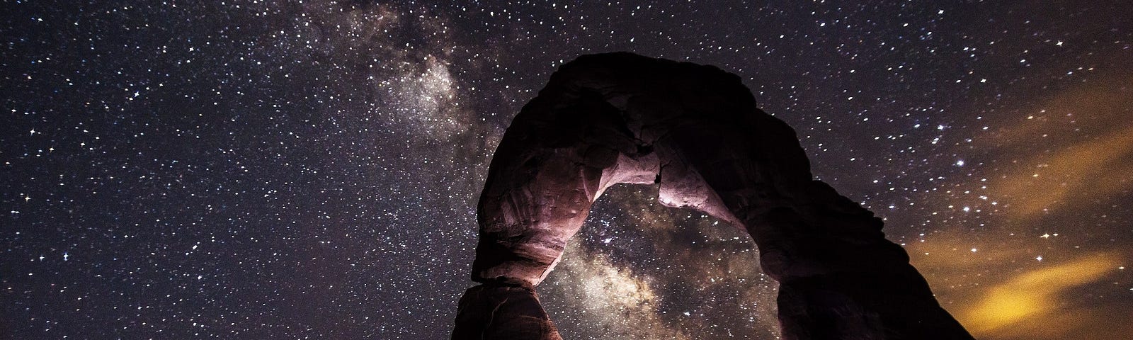 Person under rocky arch with night sky above them.