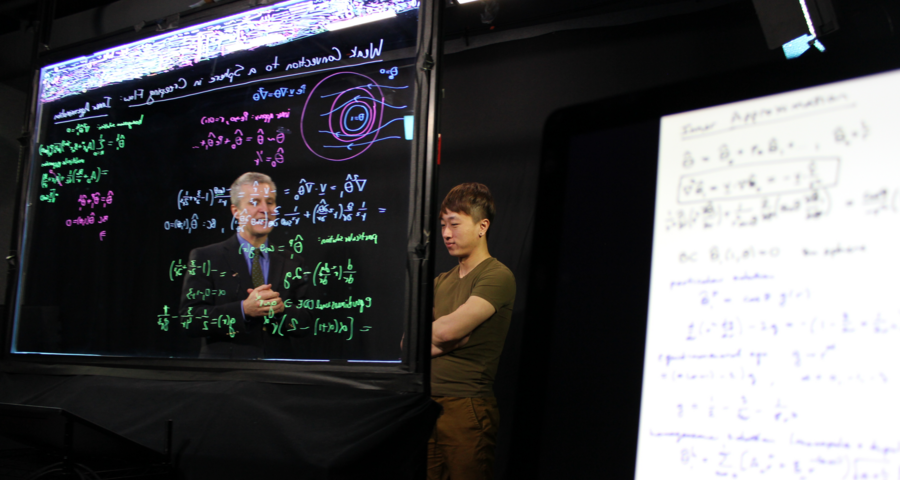 Photo of two educators discussing equations on a lightboard in front of them.