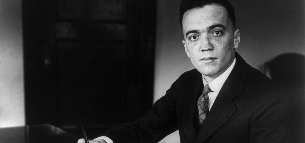 J. Edgar Hoover sitting a desk with a pen in his hand