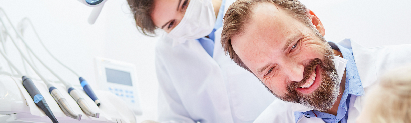 Stock image of a child in a dentist’s chair with a dentist and dental hygienist smiling while conversing with the child.