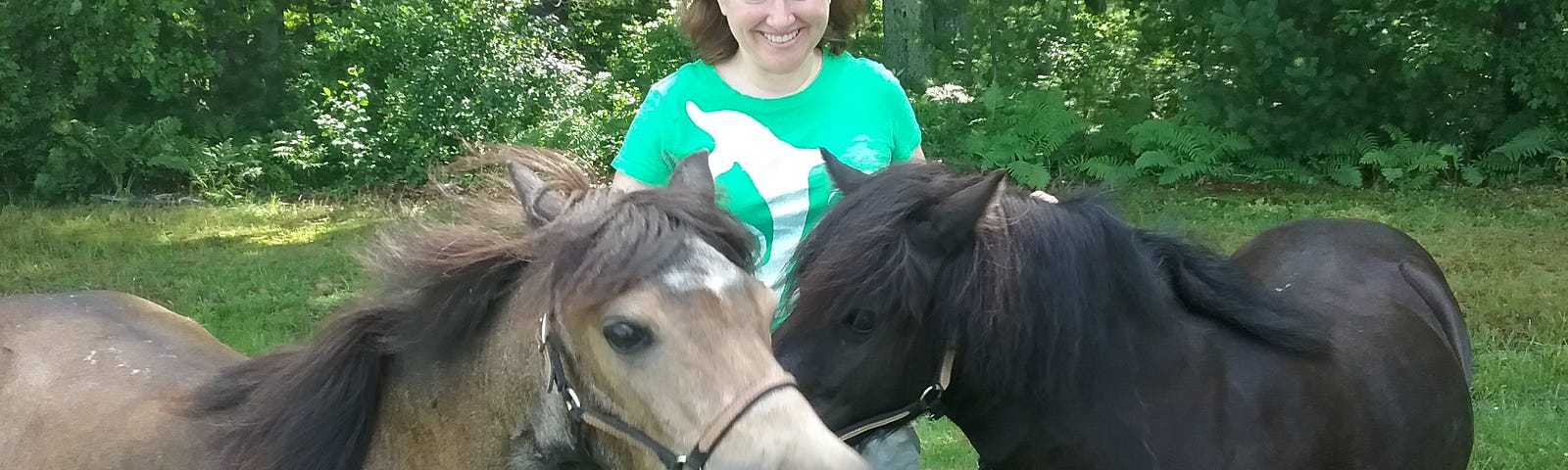 a woman smiles and stands with two small horses