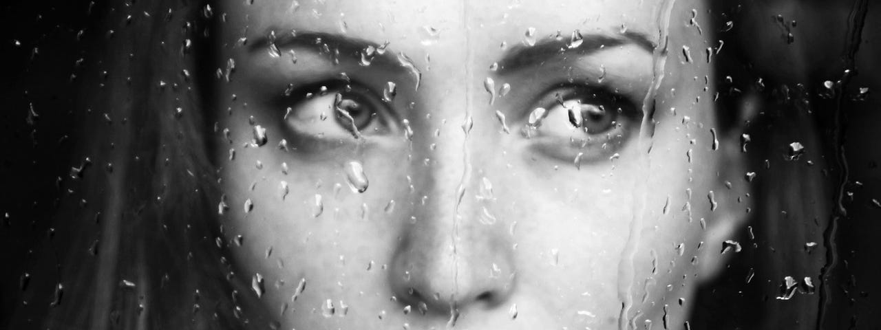 Woman looking sad through glass with rain drops on it.
