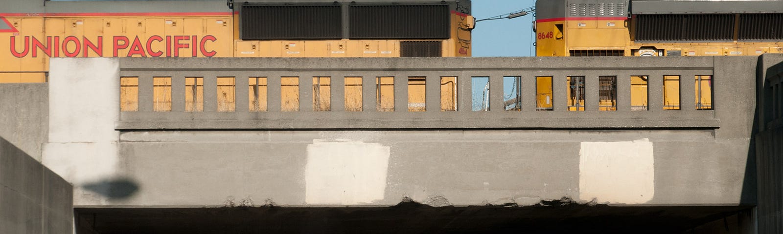 Two yellow partially-seen Union Pacific locomotives crossing an old beaten-up-looking grey concrete bridge.