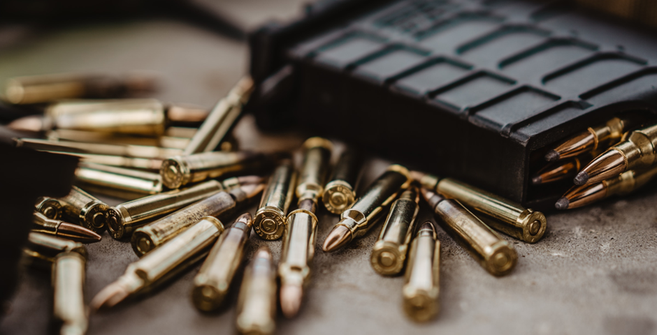 Shiny brass-colored bullets strewn haphazardly on a table next to a grey cartridge loaded with the same ammunition.