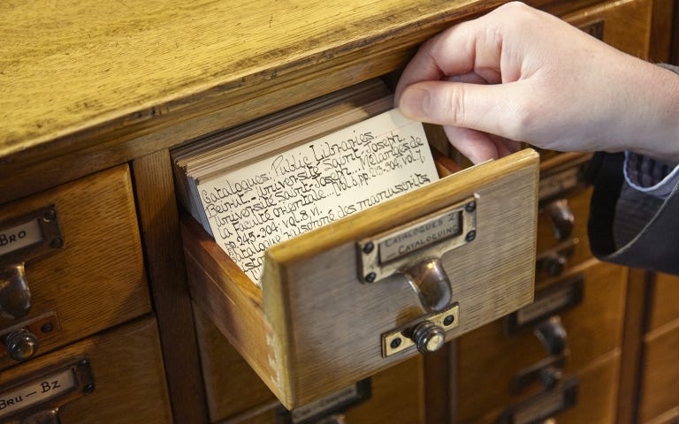 Hand lifting a paper card out of a card catalogue.