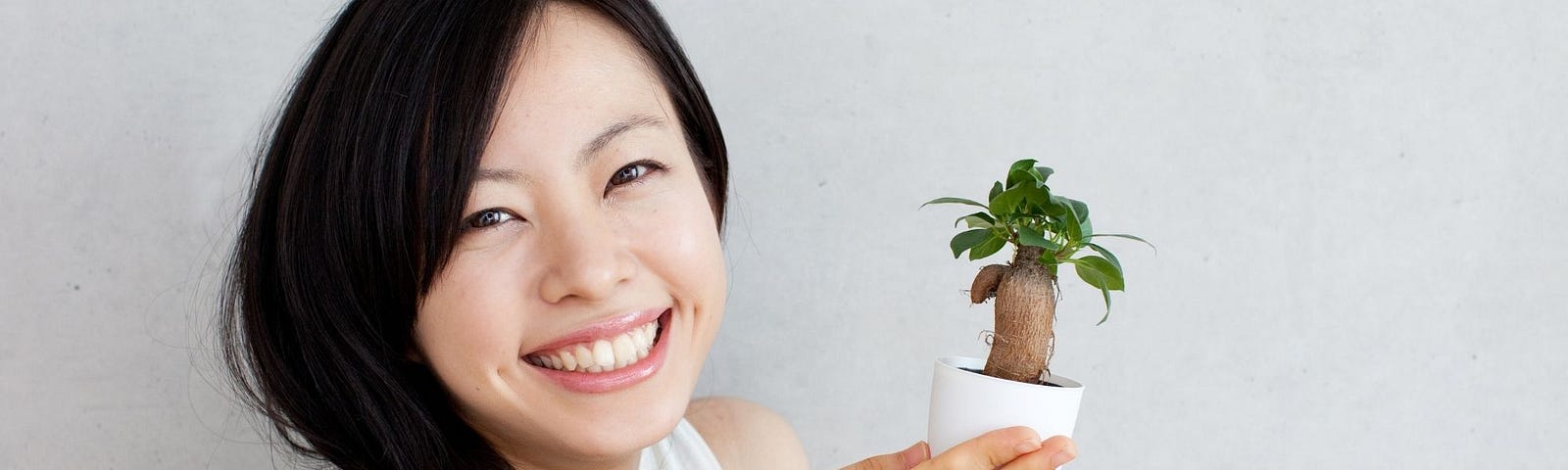 A smiling Asian woman holding a tiny house plant