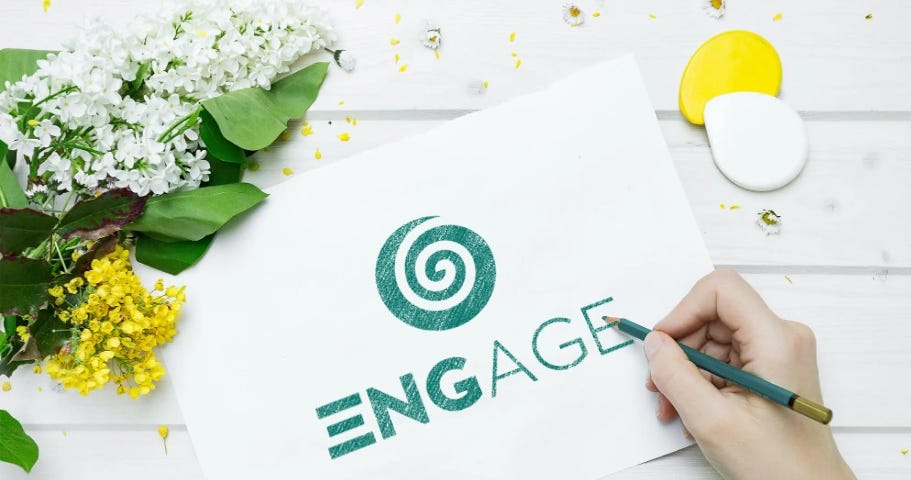 A writer’s hand writing “Engage” on a sheet of paper with green ink with flowers on the right upper corner.