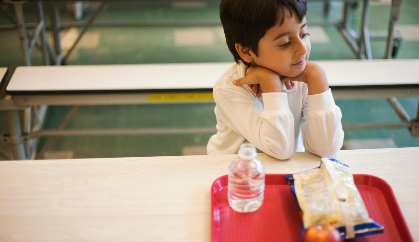 Student sits at lunch table with tray of food.