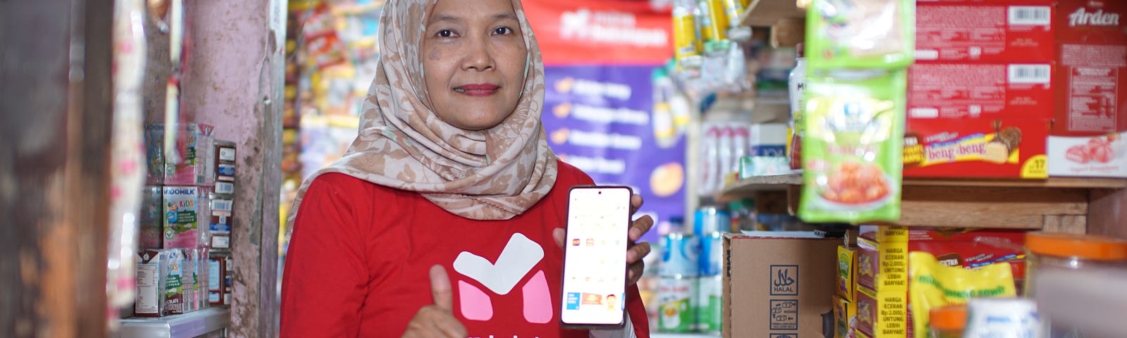 Ibu Retno stands in her store and demonstrates the Mitra Bukalapak application on her smartphone.