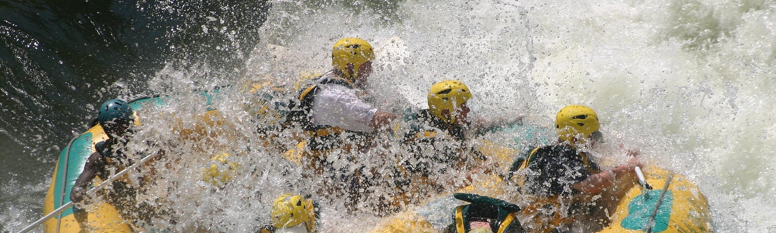 Inflatable raft with helmeted paddlers in white-water river.