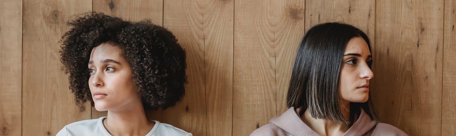 Pensive multiracial women near wooden wall looking away