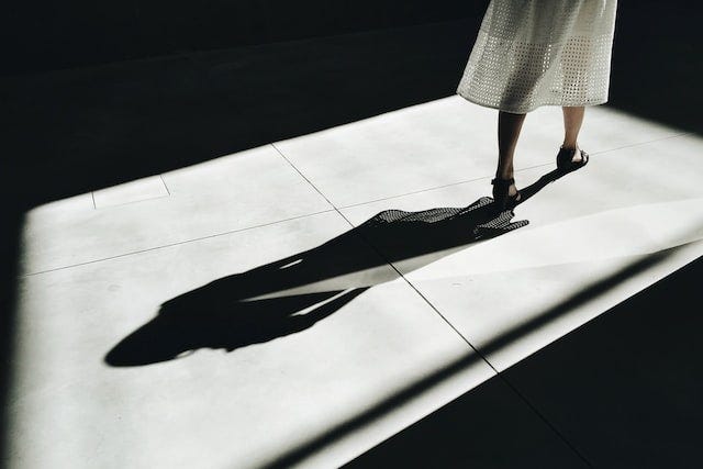 black and white picture of a shadow behind a persons body, reflected on the ground.